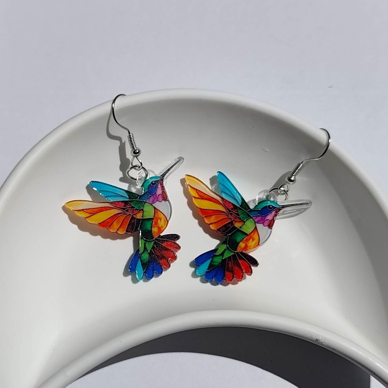 Colorful hummingbird-shaped earrings on a white dish